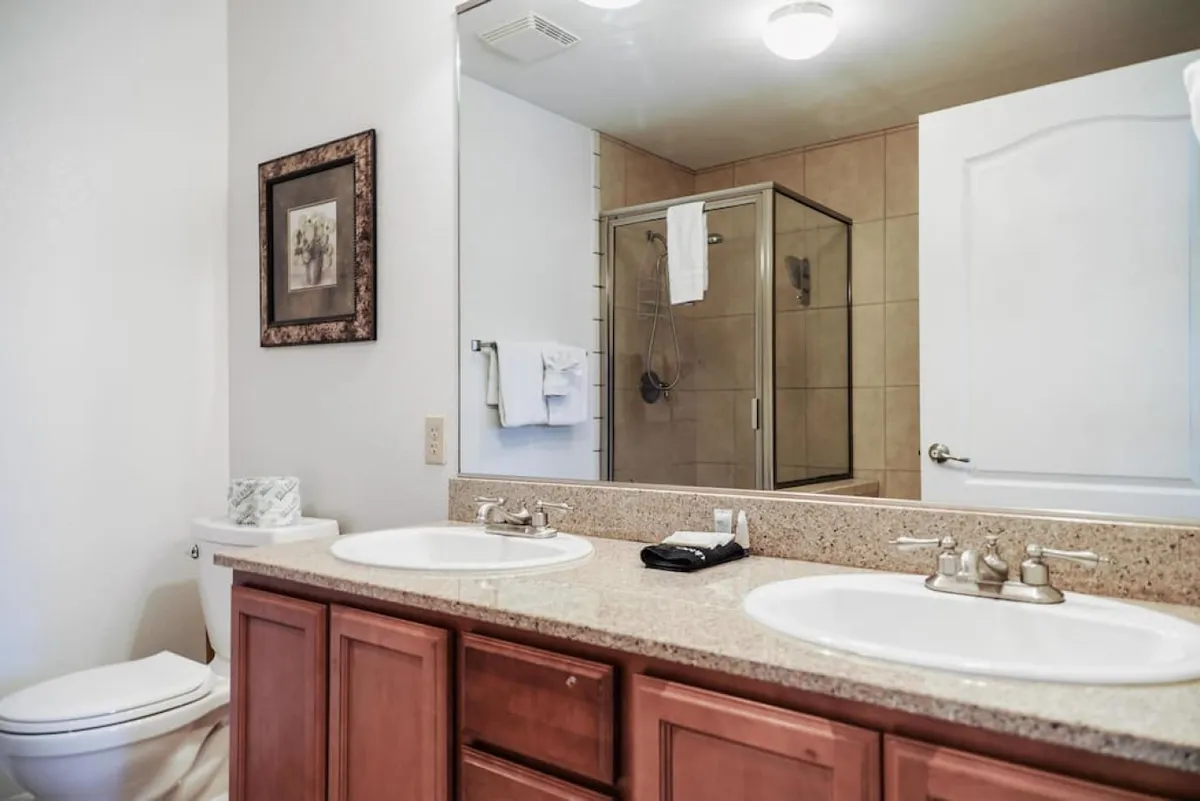 A spacious and modern bathroom featuring double vanity sinks, a glass shower enclosure, and tasteful framed artwork. The clean lines and soft lighting emphasize an inviting, spa-like atmosphere.