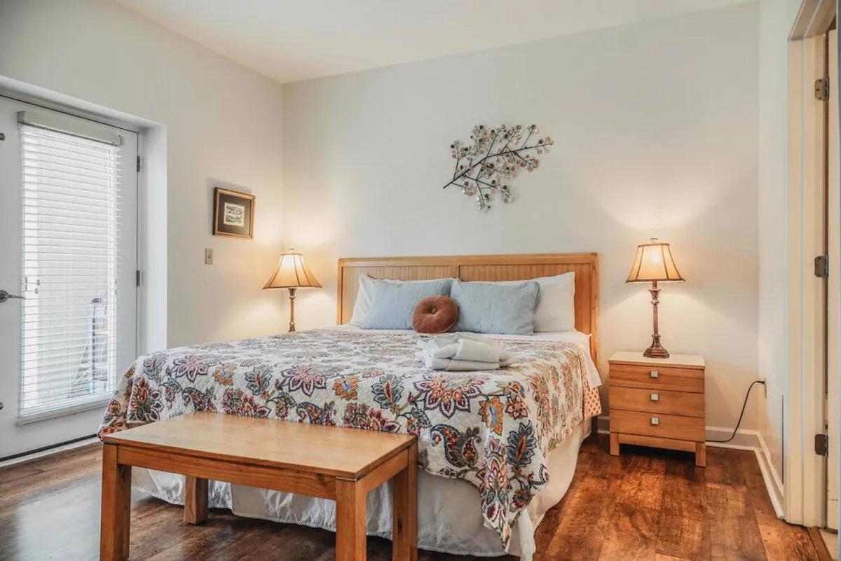 A peaceful bedroom featuring a bed with decorative bedding, two nightstands with lamps, a wooden bench at the foot of the bed, and sunlight streaming through the window. The room exudes comfort and a sense of relaxation, ideal for a restful night's sleep.