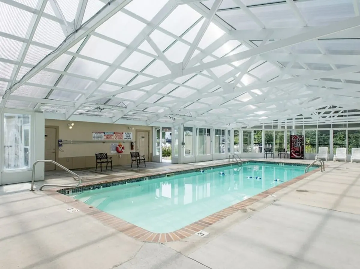 This image displays an inviting indoor swimming pool with a translucent roof allowing natural light to brighten the space. Comfortable seating lines the poolside, creating a cheerful, social atmosphere perfect for year-round fun regardless of the weather.