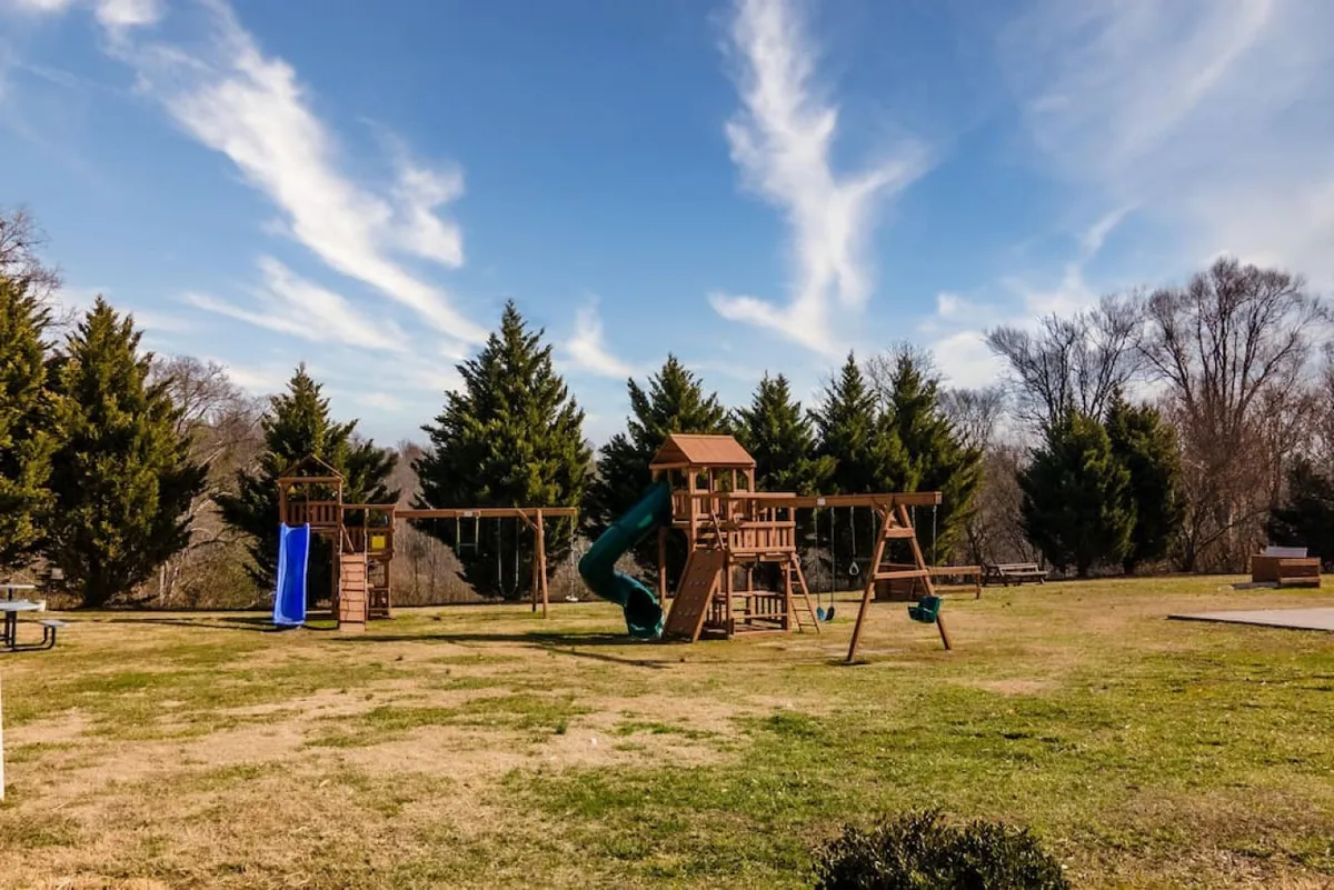 The photo showcases a colorful playground complete with a slide, swings, and a picnic area, all set against a backdrop of green grass and trees. Children are seen playing, and nearby benches invite family gatherings or quiet moments for parents.