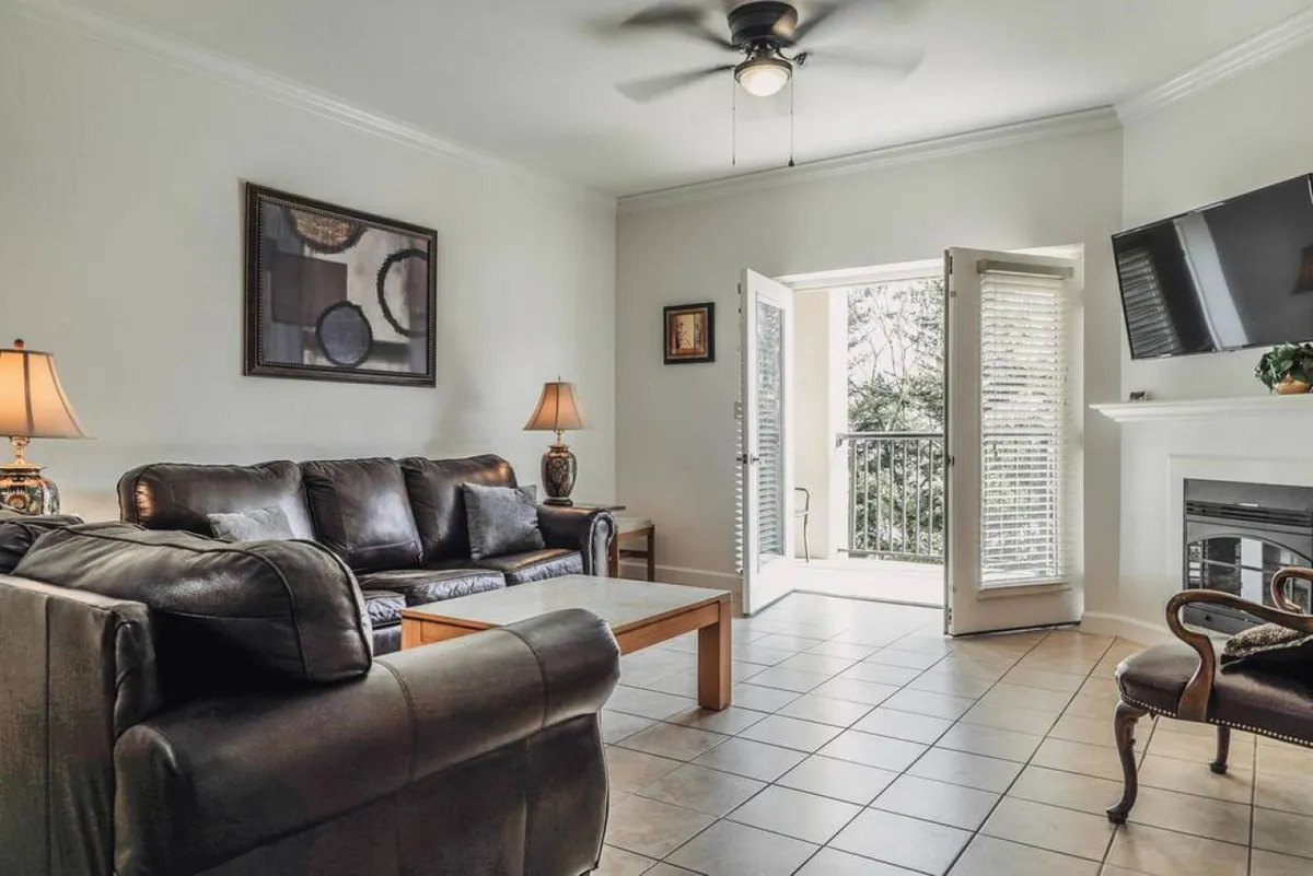 A living room setting with an inviting sofa, coffee table, lamp, fireplace, and open doors that lead outside, suggesting seamless indoor-outdoor living. The ambiance is warm and cozy, ideal for relaxing after a day of exploring local attractions.