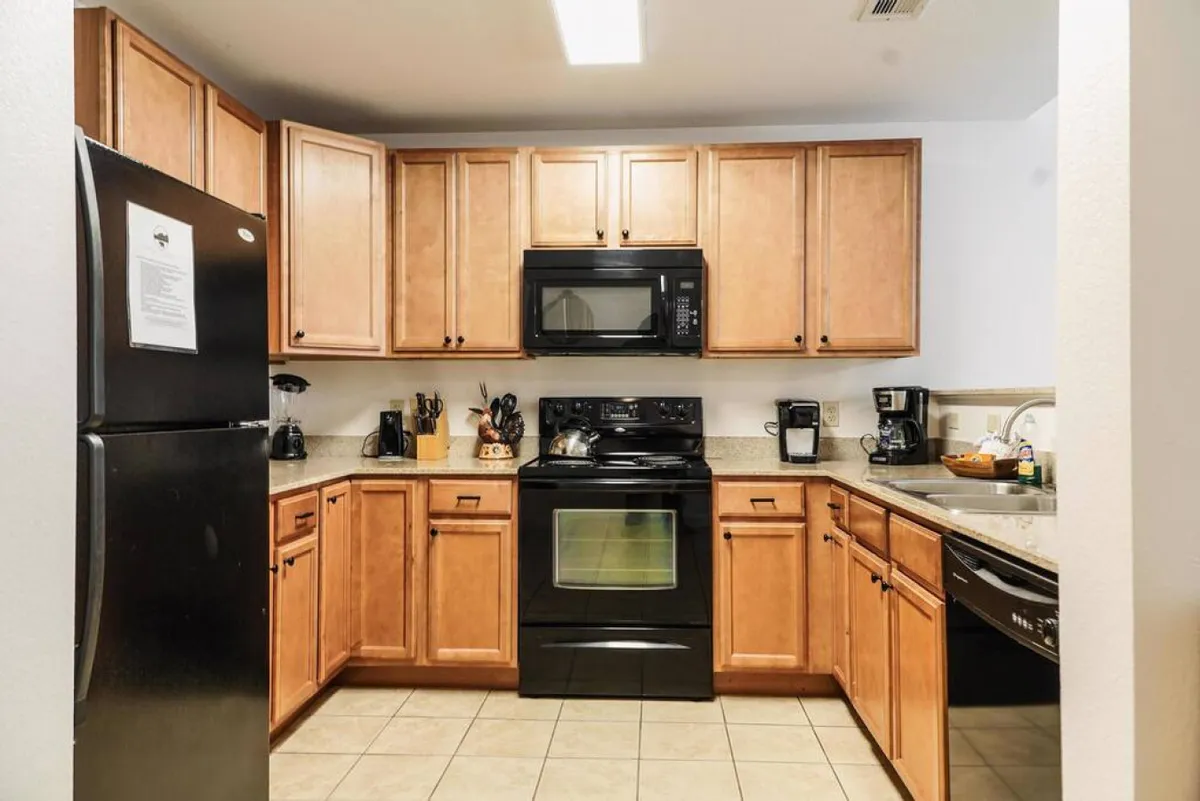 A modern kitchen featuring black appliances, wooden cabinets, and granite countertops. Kitchen utensils are visible, suggesting the space is ready for cooking and meal prep. The kitchen looks inviting and practical, with everything in easy reach for daily culinary adventures.