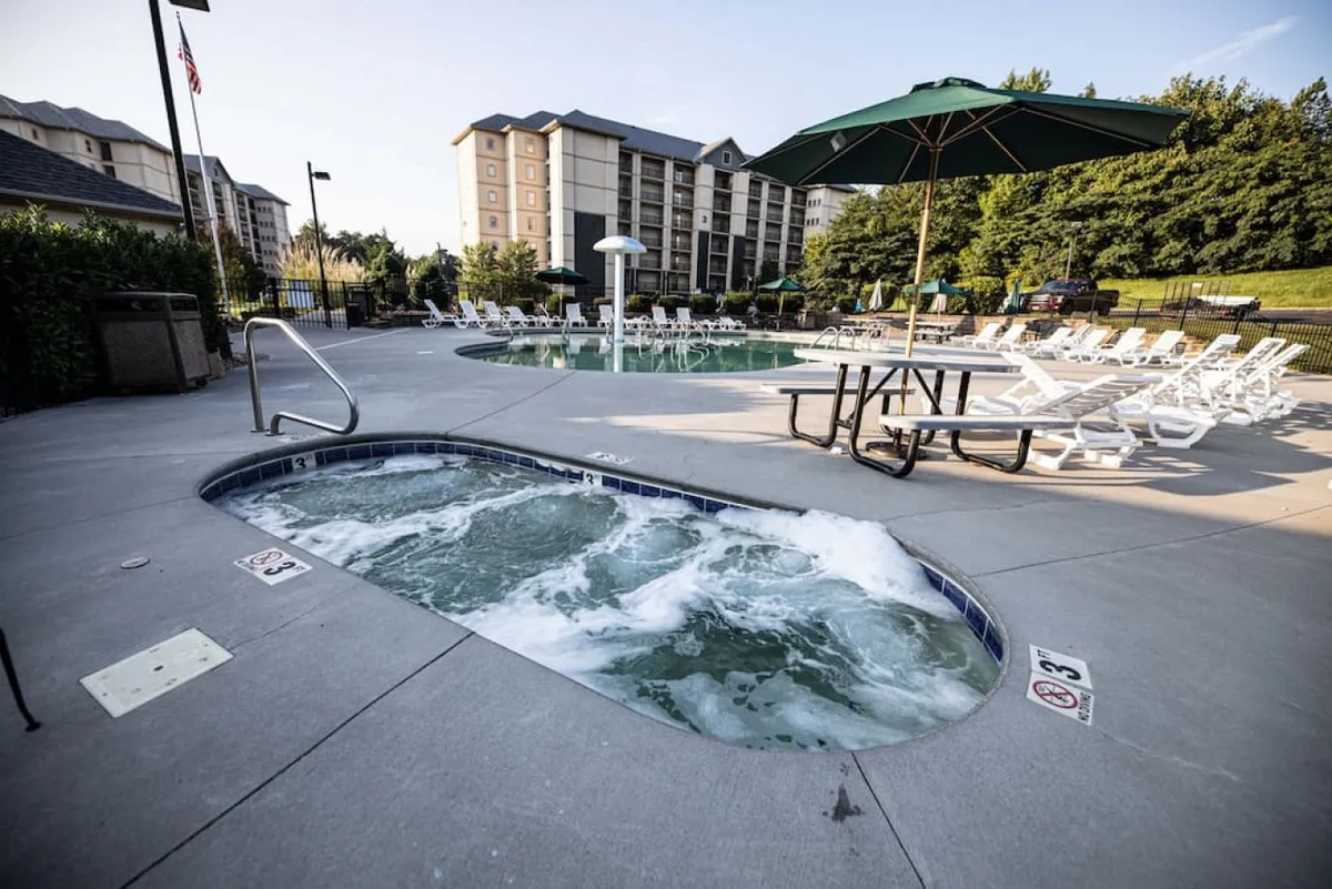 An exterior shot of the swimming pool area, featuring a hot tub, lounge chairs, umbrella-covered tables, and sunset lighting. The mood is leisurely and social, hinting at relaxation and outdoor enjoyment within the property grounds.