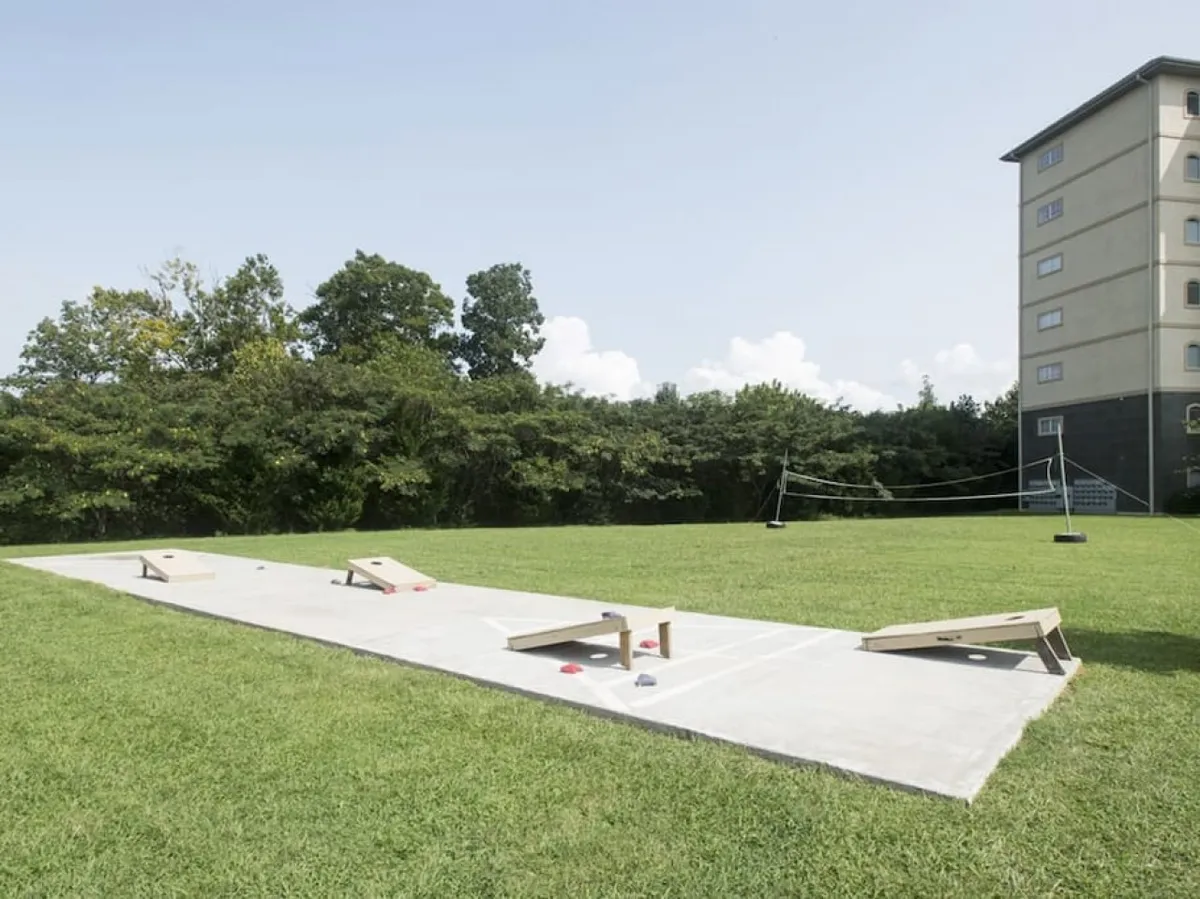 This vibrant exterior shot captures a lush lawn with cornhole boards, a volleyball net, and a multi-story building in the background. The scene is set for friendly competitions, picnics, and social gatherings, highlighting the resort's broad range of outdoor sports and leisure activities.