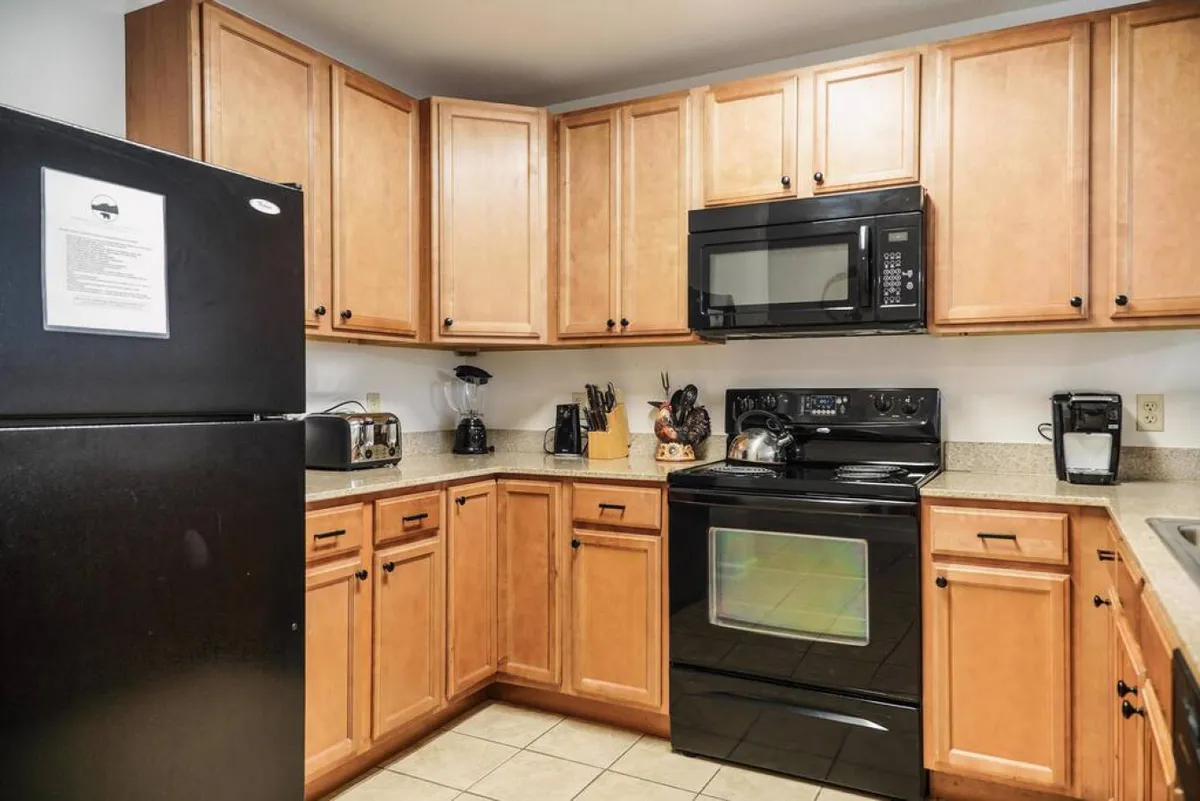 A close-up view of the kitchen, highlighting a black refrigerator, stainless steel microwave, granite countertop, wooden cabinets, and a variety of kitchen utensils. The space feels cozy and well-stocked for preparing meals and snacks.