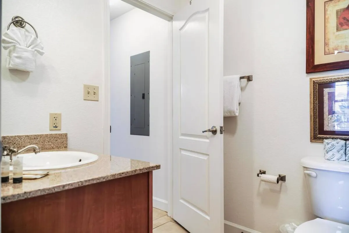 A fresh and inviting full bathroom with a sink, countertop, toilet, plush towels, and framed artwork. The layout is practical yet stylish, perfect for personal grooming and added convenience for families or groups.