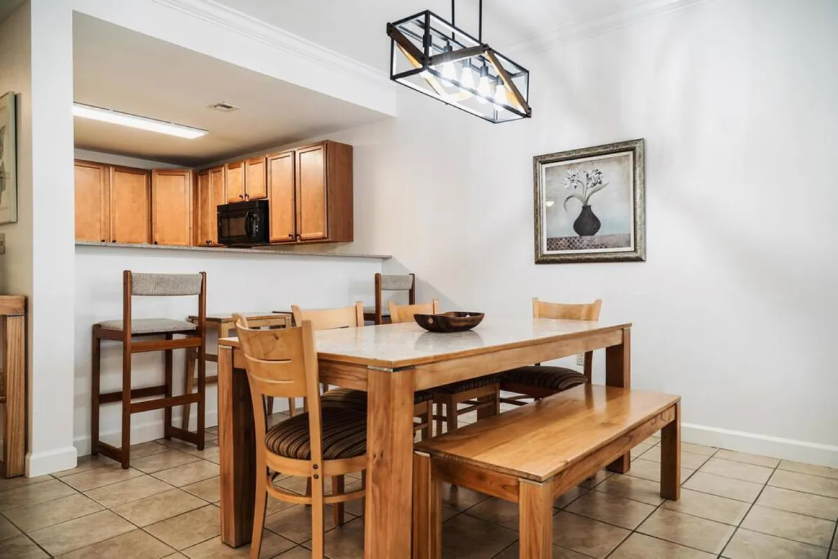 A cozy dining nook with a wooden table set under a warm hanging light fixture, complemented by framed artwork and a glimpse of the kitchen counter. The layout encourages shared meals, board games, or family celebrations.