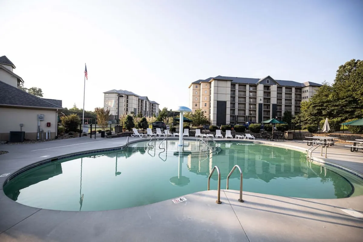 This image depicts a sparkling outdoor swimming pool surrounded by lounge chairs, with landscaped gardens and nearby resort buildings visible, creating a lively and inviting atmosphere for families. The pool area is sunlit, evoking a sense of fun, relaxation, and togetherness.