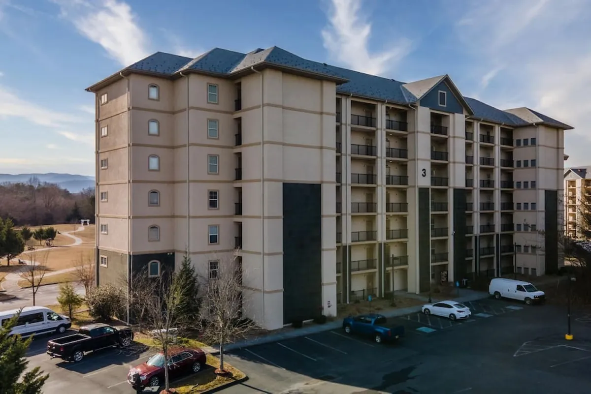 This image showcases the exterior of the condo building, featuring the parking area, landscaped surroundings, and a backdrop of stunning mountain views. The scene is calm and welcoming, highlighting the property's location within a vibrant yet tranquil setting.